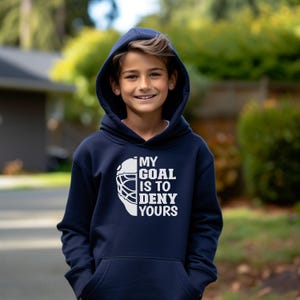 Peut inclure: Un sweat &agrave; capuche bleu marine avec un graphique blanc d'un masque de gardien de hockey et le texte "My Goal Is To Deny Yours".