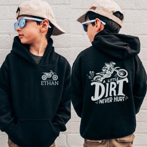 May include: Black hoodie with a front pocket and a drawstring hood. The front features a white motorcycle graphic and the name "ETHAN". The back displays a motorcycle graphic with the text "A LITTLE DIRT NEVER HURT".