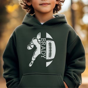 May include: Dark green hoodie with a white graphic of a football player and the name "BRADY" in white. The design is a football with the player inside. The hoodie has a front pocket and a hood.