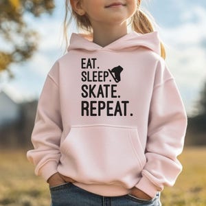 May include: Pink hooded sweatshirt with the text "Eat. Sleep. Skate. Repeat." and a silhouette of a person ice skating.