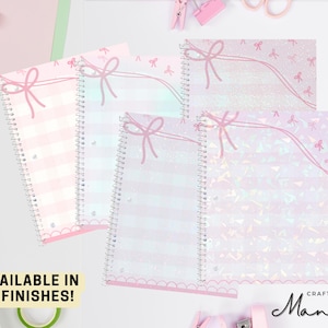 May include: Five different pastel-colored spiral notebooks with a pink bow design and iridescent glitter. The notebooks have the text "Crafty Mandy" on the bottom right corner.  AVAILABLE IN 5 FINISHES! is written at the bottom left corner.
