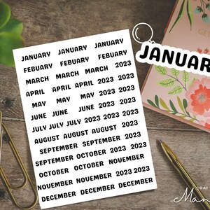 May include: A sheet of white sticker paper with black text. The stickers are for each month of the year 2023. The text on the stickers reads: January, February, March, April, May, June, July, August, September, October, November, December.