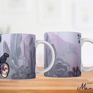 Könnte beinhalten: Zwei weiße Keramikbecher mit einem lila, grauen und schwarzen Design. Ein Becher zeigt einen schwarzen Raben, der auf einem Schädel mit rosa Blumen sitzt. Der andere Becher zeigt ein Aquarelldesign einer Rose mit rosa und grauen Blumen.