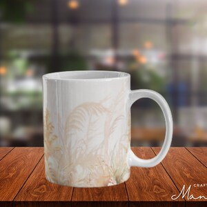 Könnte beinhalten: Weiße Keramiktasse mit beigefarbenem Blumendesign. Die Tasse hat einen abgerundeten Griff und einen breiten Boden.