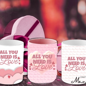 Könnte beinhalten: Drei weiße Keramikbecher mit rosa und roten Herzen und dem Text "All You Need Is Love" darauf gedruckt. Die Becher stehen auf einem rosa und weißen Hintergrund.