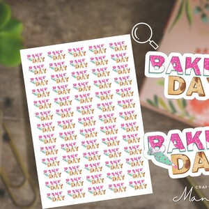 Peut inclure: Une feuille d'autocollants avec les mots "Bake Day" répétés plusieurs fois. Les autocollants sont roses et bruns avec un design glaçage de beigne. Il y a deux autocollants plus grands avec les mots "Bake Day" dans un design similaire.
