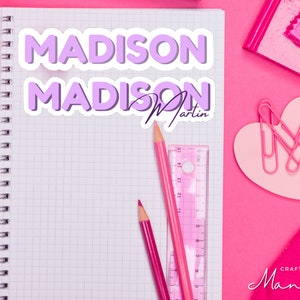 Peut inclure: Un carnet rose avec une grille blanche et une reliure spirale. Le carnet a deux autocollants sur le devant, tous deux avec le nom "MADISON" en lettres violettes. L'autocollant du bas a également le texte "Martin" en lettres violettes plus petites. Le carnet est entouré de fournitures scolaires roses et blanches, y compris un crayon rose, une règle rose, un porte-trombones en forme de cœur rose et un taille-crayon rose.