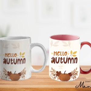 Könnte beinhalten: Zwei weiße Keramikbecher, einer mit rotem Henkel. Beide Becher haben ein Herbstmotiv mit dem Text "Hello autumn" und einer kleinen Kürbisillustration.