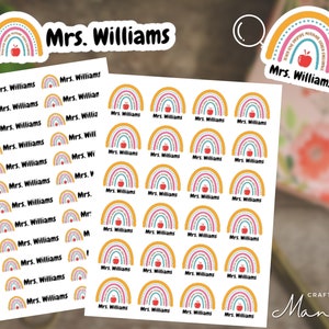 Peut inclure: Une feuille de 24 autocollants personnalisés sur le thème de l'arc-en-ciel avec le texte "Mrs. Williams" sur chaque autocollant. L'arc-en-ciel est composé de bandes jaunes, orange, roses, bleues et vertes avec des pois blancs. Chaque arc-en-ciel a une pomme rouge au centre.