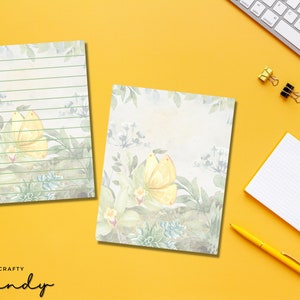 May include: Two printable stationery sheets with a watercolour background featuring green leaves, white flowers, and yellow butterflies. The top sheet has green lines for writing.