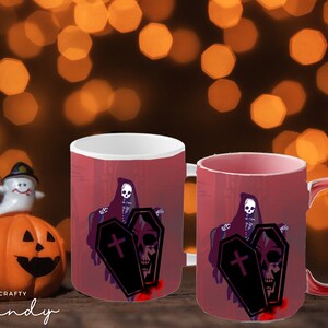 Könnte beinhalten: Zwei rote Kaffeetassen mit Halloween-Motiv. Die Tassen zeigen ein Skelett in einer Kapuzenrobe, das zwei Särge hält. Ein Sarg hat ein Kreuz darauf und der andere einen Schädel. Der Hintergrund ist ein verschwommenes Bild von orangefarbenen Lichtern.