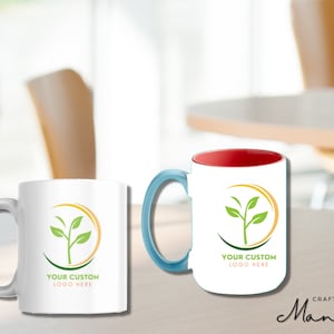 Könnte beinhalten: Zwei weiße Keramikbecher mit einem blauen und roten Griff. Beide Becher zeigen ein grünes Pflanzenlogo mit dem Text "YOUR CUSTOM LOGO HERE" auf einem gelben Kreis.