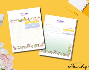 Puede incluir: Dos blocs de notas de planificación diaria blancos con detalles florales y de mariposas. Cada bloc de notas tiene secciones para listas de tareas, recordatorios y notas. El texto "The Daily" está en la parte superior de cada bloc.