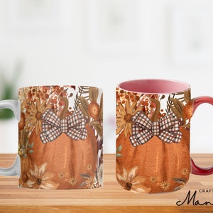 Könnte beinhalten: Eine weiße Keramiktasse mit rotem Henkel zeigt ein Herbstmotiv. Das Design beinhaltet einen Kürbis mit einer karierten Schleife, umgeben von orangefarbenen, braunen und gelben Blumen. Der Text "Crafty Mandy" ist am Boden der Tasse sichtbar.