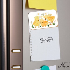 May include: A rectangular magnet with a watercolour illustration of three yellow chicks and floral details. A notepad with the text "call jenny 505-0012" is attached to a refrigerator.