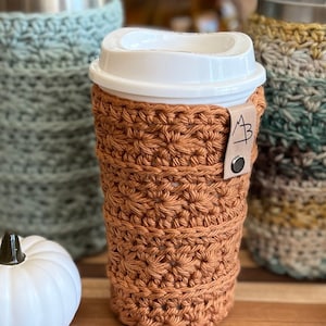 Pu&ograve; includere: Un copri-tazza da caff&egrave; all'uncinetto di colore arancio bruciato con un cinturino in pelle marrone con le iniziali "A B".