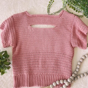 May include: A pink crocheted top with short sleeves and a keyhole cutout in the back.