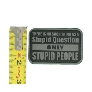 May include: A rectangular patch with the text "THERE IS NO SUCH THING AS A Stupid Question ONLY STUPID PEOPLE" in white and gray. A yellow Stanley measuring tape is next to the patch, showing 2 inches.