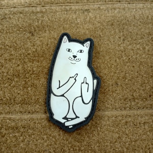 May include: White cat patch with black outline, sitting with a middle finger raised. The cat has a mischievous expression on its face.