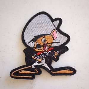 May include: An embroidered patch featuring a cartoon mouse wearing a sombrero and holding a gun. The mouse is brown and white, and the sombrero is white with a black trim. The gun is black and has a brown handle.