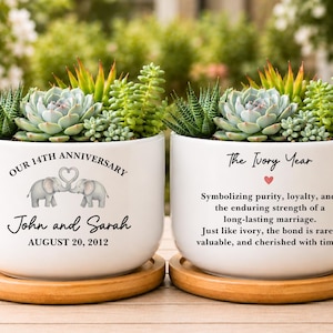 May include: Two white ceramic planters on bamboo saucers, each filled with assorted green succulents. The left planter features two elephants forming a heart with their trunks, the text "OUR 14TH ANNIVERSARY", "John and Sarah", and "AUGUST 20, 2012".