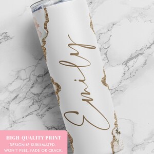 May include: White stainless steel tumbler with a gold glitter and floral design. The tumbler has the name "Emily" written in cursive on the front.