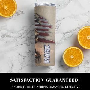 May include: A stainless steel tumbler with a patriotic design featuring a torn American flag and the word "MARK" printed on the side. The tumbler is on a white marble surface with oranges.