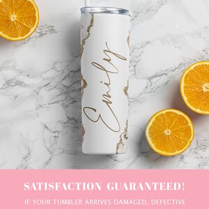 May include: White stainless steel tumbler with a gold glitter design and the name "Emily" written in cursive. The tumbler is sitting on a white marble surface with three orange slices.