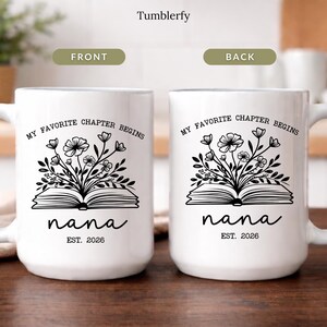 K&ouml;nnte beinhalten: Zwei wei&szlig;e Keramikbecher mit dem Text "MY FAVORITE CHAPTER BEGINS" und "nana EST. 2026". Jeder Becher hat ein schwarzes Blumendesign &uuml;ber einem offenen Buch. Die Becher stehen auf einer Holzoberfl&auml;che.