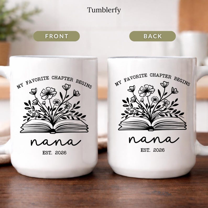 K&ouml;nnte beinhalten: Zwei wei&szlig;e Keramikbecher mit dem Text "MY FAVORITE CHAPTER BEGINS" und "nana EST. 2026". Jeder Becher hat ein schwarzes Blumendesign &uuml;ber einem offenen Buch. Die Becher stehen auf einer Holzoberfl&auml;che.