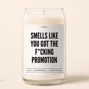 May include: A clear glass jar candle filled with white soy wax. The label features the text Tumblerfy and Smells Like You Got The F*cking Promotion in black font. The label also displays 13.75 oz, 60-80 hours burn time, and 100% soy wax candle.