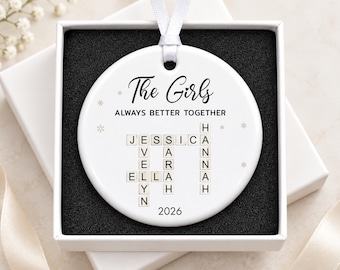 May include: A round white ceramic ornament featuring a white ribbon hanger. The text reads The Girls ALWAYS BETTER TOGETHER and 2026. A crossword-style grid displays the names Jessica, Evelyn, Sarah, Ella, and Hannah with small snowflake accents.