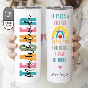 May include: White insulated tumbler with colorful text and graphics. One side reads "Mrs. Whiteside" in black script over colorful blocks. The other side says "It takes a village" with a rainbow and apple graphic. A heart and the name "Skyla" are also included.