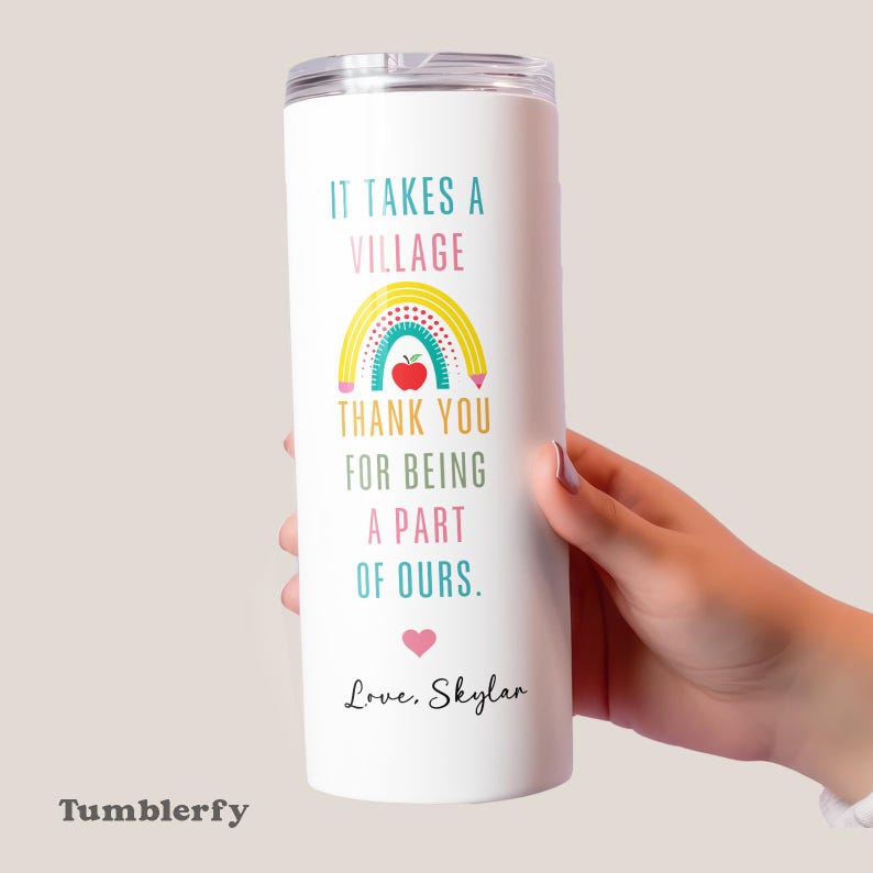 May include: White tumbler with a clear lid featuring the text "IT TAKES A VILLAGE" and "THANK YOU FOR BEING A PART OF OURS." A rainbow, apple, and heart graphic are included. The name "Love, Skylar" is also printed on the tumbler.