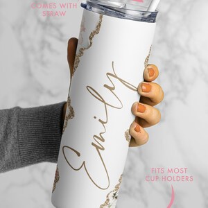 May include: White stainless steel tumbler with a gold glitter design and the name "Emily" written in cursive. The tumbler comes with a straw and fits most cup holders.