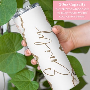 May include: White tumbler with a gold glitter design and the name "Emily" written in cursive. The tumbler is 20 ounces and is perfect for cold or hot drinks.