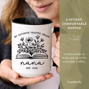 K&ouml;nnte beinhalten: Wei&szlig;er Keramikbecher mit schwarzem Innenraum und Griff. Der Becher tr&auml;gt den Text "MY FAVORITE CHAPTER BEGINS" und "nana EST. 2026" mit einem floralen und Buch-Design. Ein robuster, komfortabler Griff ist sichtbar.