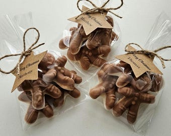 May include: Three clear cellophane bags tied with twine, each containing gingerbread men candies. Each bag has a star-shaped tag with a name and the words "Merry Christmas". The candies are light brown.