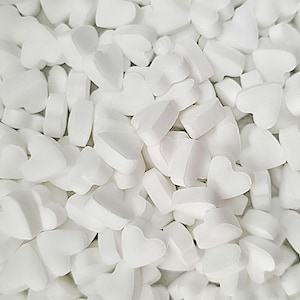 May include: A close-up shot of a pile of white, heart-shaped packing peanuts. The foam pieces are scattered, creating a textured surface. The shapes vary slightly, with some appearing more rounded than others.