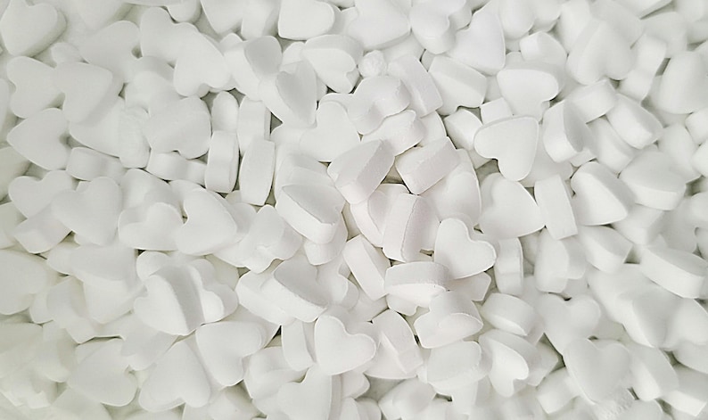 May include: A close-up shot of a pile of white, heart-shaped packing peanuts. The foam pieces are scattered, creating a textured surface. The shapes vary slightly, with some appearing more rounded than others.