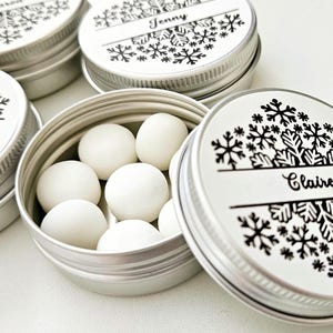 May include: Six silver round tins with snowflake designs and personalised names. The tins are filled with white mints.