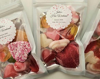 May include: Three clear plastic bags filled with colorful candies. Each bag has a white circle sticker with the text "Julie's Hen Weekend" and the date "January 2023".