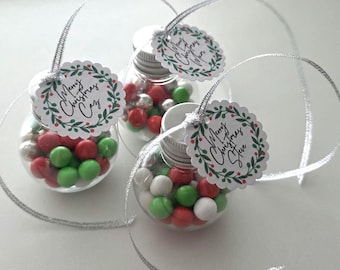 May include: Three clear spherical plastic ornaments filled with red, green, and silver candies. Each ornament has a silver screw-top lid, a silver hanging ribbon, and a scalloped white tag featuring a green wreath and the text Merry Christmas.