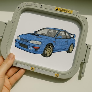 May include: Embroidered patch featuring a blue sports car with gold wheels. The car has a spoiler and is set against a white background. The patch is held in a gray embroidery hoop with warning labels.