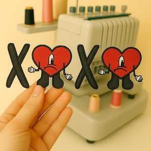Pode incluir: Patches bordados com um coração vermelho com um rosto triste, pernas pretas e mãos brancas, juntamente com letras "X" pretas. Os patches são provavelmente para roupas ou acessórios.