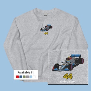 Peut inclure: Un sweat à manches longues gris avec une petite image brodée d'une voiture de course bleue et rouge avec le numéro 44. Le sweat-shirt est disponible en rouge, bleu marine, vert olive, gris et bleu clair. L'image montre également une version plus grande du motif brodé avec le texte "Broderie !" en dessous.