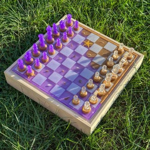 May include: A handcrafted chess set with a wooden frame and a purple and gold resin board. The chess pieces are clear with gold bases and purple tops. The board features a starfish and other decorative elements.