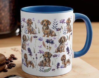 May include: White ceramic coffee mug with a blue rim and handle. The mug features a repeating pattern of dachshund dogs and purple flowers on a white background.