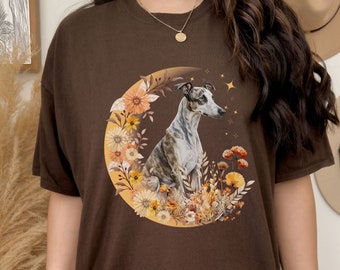 May include: A brown t-shirt featuring a graphic of a greyhound dog sitting in a crescent moon surrounded by yellow and orange flowers.