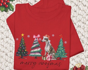 May include: A red t-shirt featuring a watercolor illustration of a dog wearing a Santa hat, sitting between decorated Christmas trees. The text "merry woofmas" is written below the trees. The shirt is folded.